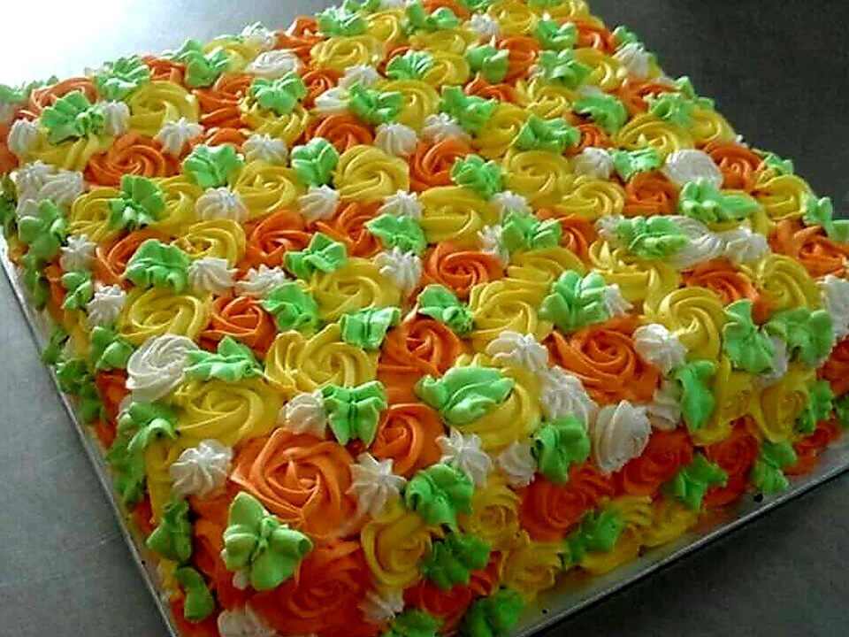 A large Mr Bake cake covered in orange, green and yellow piped cream flowers.